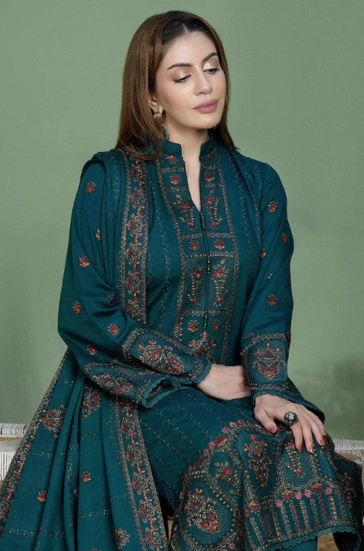 A woman modeling a traditional three-piece salwar kameez suit in deep teal green multicolor embroidery in red, gold, and beige on the kurta, pants, and matching dupatta