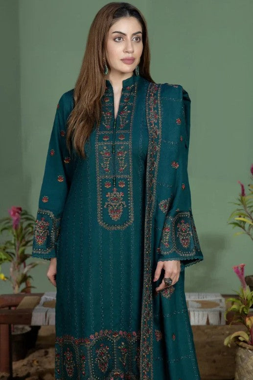 A woman modeling a traditional three-piece salwar kameez suit in deep teal green multicolor embroidery in red, gold, and beige on the kurta, pants, and matching dupatta